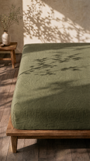 Moss linen fitted sheet on wooden bed frame with dappled sunlight shadows