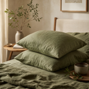 Moss green linen pillowcase set styled on wooden bed with relaxed drape and bedroom decor