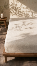 Oat linen fitted sheet styled on wooden bed frame in sunlit bedroom