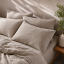 Three oat linen pillowcases propped against headboard
