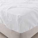 White fitted linen sheet snugly draped over beige upholstered bed base with visible corner seam