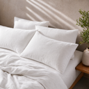 Soft white linen pillowcase set styled on a bed with natural sunlight